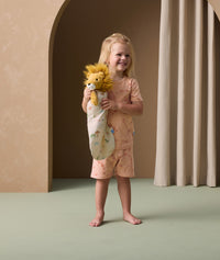 A preschooler is wearing short-sleeve pyjamas with an elephant print while holding a plush lion dressed in a doll-sized sleeping bag.
