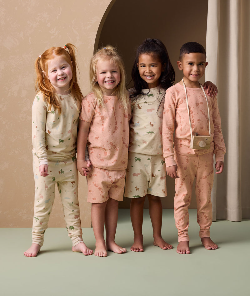Four preschoolers stand smiling together, wearing coordinating ergoPouch long sleeve and short sleeve pyjamas with playful animal prints