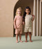 Two preschoolers stand next to each other while holding hands. They both wear ergoPouch Short Sleeve Pyjamas in Elephant Parade and Savannah.