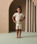 A preschooler stands confidently with hands on hips,  wearing a light beige short-sleeve pyjama set featuring a colorful safari animal print.