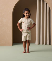 A preschooler stands confidently with hands on hips,  wearing a light beige short-sleeve pyjama set featuring a colorful safari animal print.