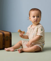 A toddler sits on the floor, holding a toy car and wearing a short-sleeved two-piece pyjama set.