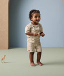 A toddler stands while holding a toy animal, wearing short-sleeve pyjamas with a safari animal print.