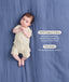 Baby lying on their back on a blue blanket wearing a cream patterned Short Sleeve Layer, next to product feature text callouts for GOTS Organic Cotton and TOG-Rating.