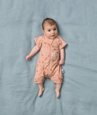 Baby is lying on a soft blue sheet, wearing an ergoPouch Short Sleeve Layer with elephant print, made from soft organic cotton gentle on baby's skin.