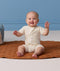 Smiling baby sitting on a brown mat with hands raised, wearing a cream patterned Short Sleeve layer.