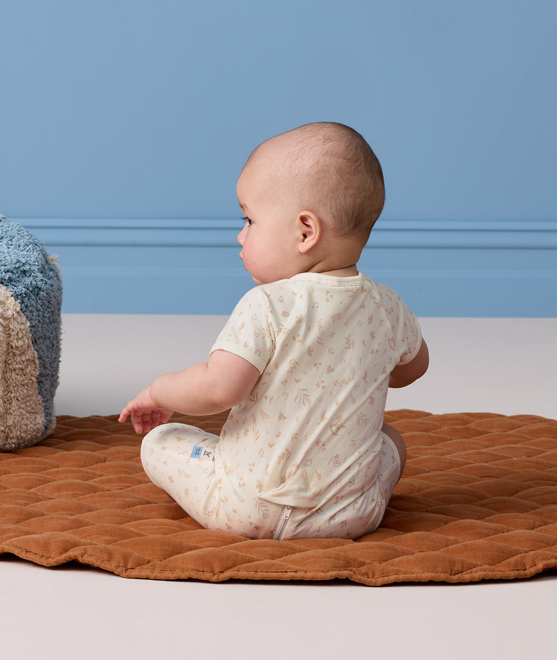 Infant sitting on a brown mat viewed from behind, wearing a cream patterned Short Sleeve Layer.