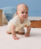 Baby crawling on hands and knees, wearing a cream patterned short-sleeve layer.