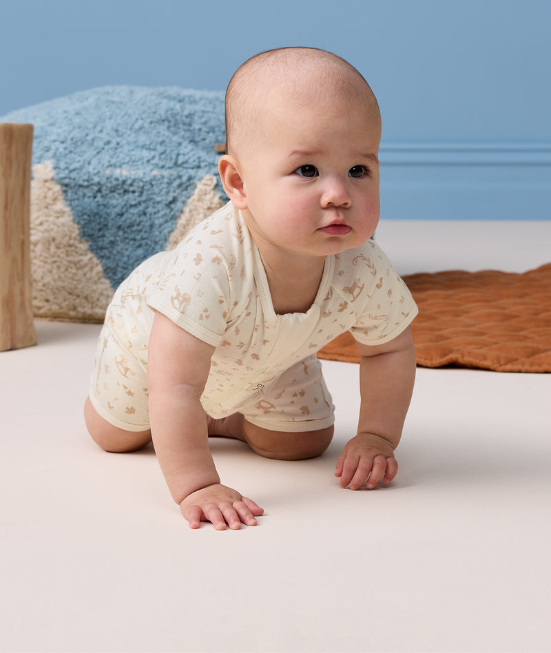 Baby crawling on hands and knees, wearing a cream patterned short-sleeve layer.