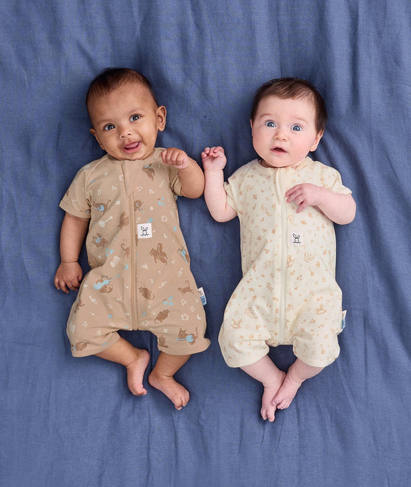 Two babies lying on a blue blanket wearing ergoPouch Short Sleeve Layers in Melody and Lullaby