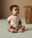 Infant sitting on the floor, wearing an ergoPouch short sleeve layer made from soft, organic cotton that is gentle on the baby's skin.