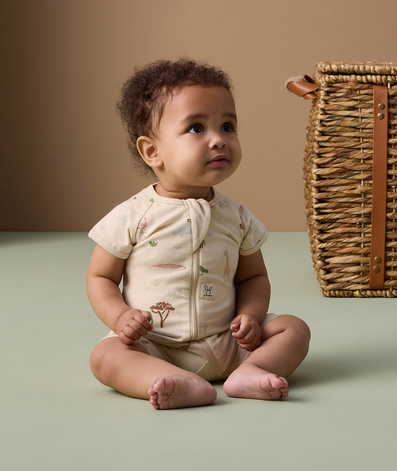 Infant sitting on the floor, wearing an ergoPouch short sleeve layer made from soft, organic cotton that is gentle on the baby's skin.
