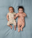 Two babies lying side by side wearing ergoPouch Short Sleeve Layer in Savannah and Long Sleeve Layer in Elephant Parade.