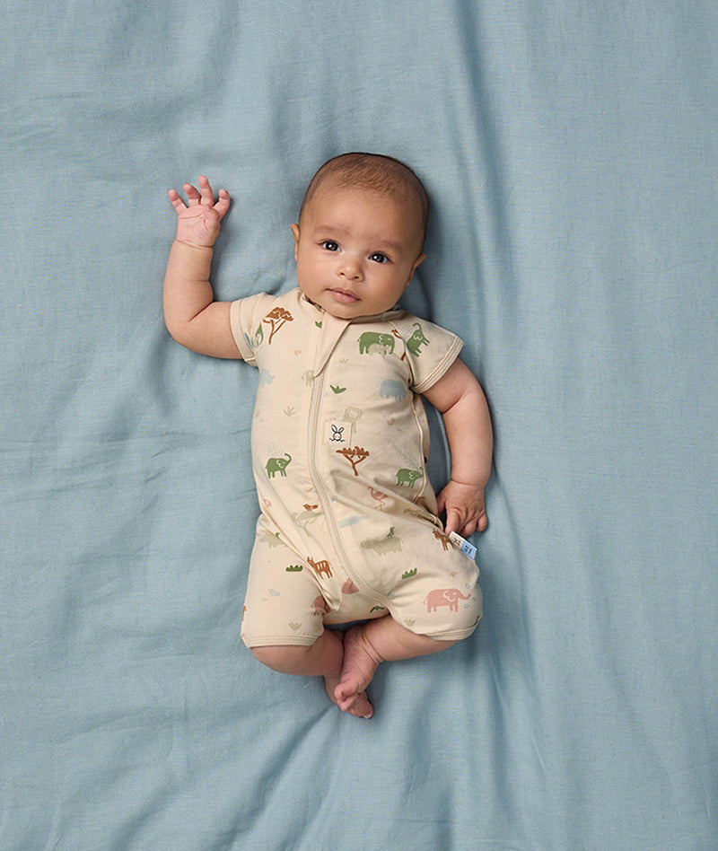 Baby lying on a soft blue sheet, wearing an ergoPouch Short Sleeve Layer, featuring a front zipper and a snug fit.