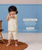 Smiling toddler standing in a cream patterned short sleeve pyjama set against a blue wall with product feature callout text.