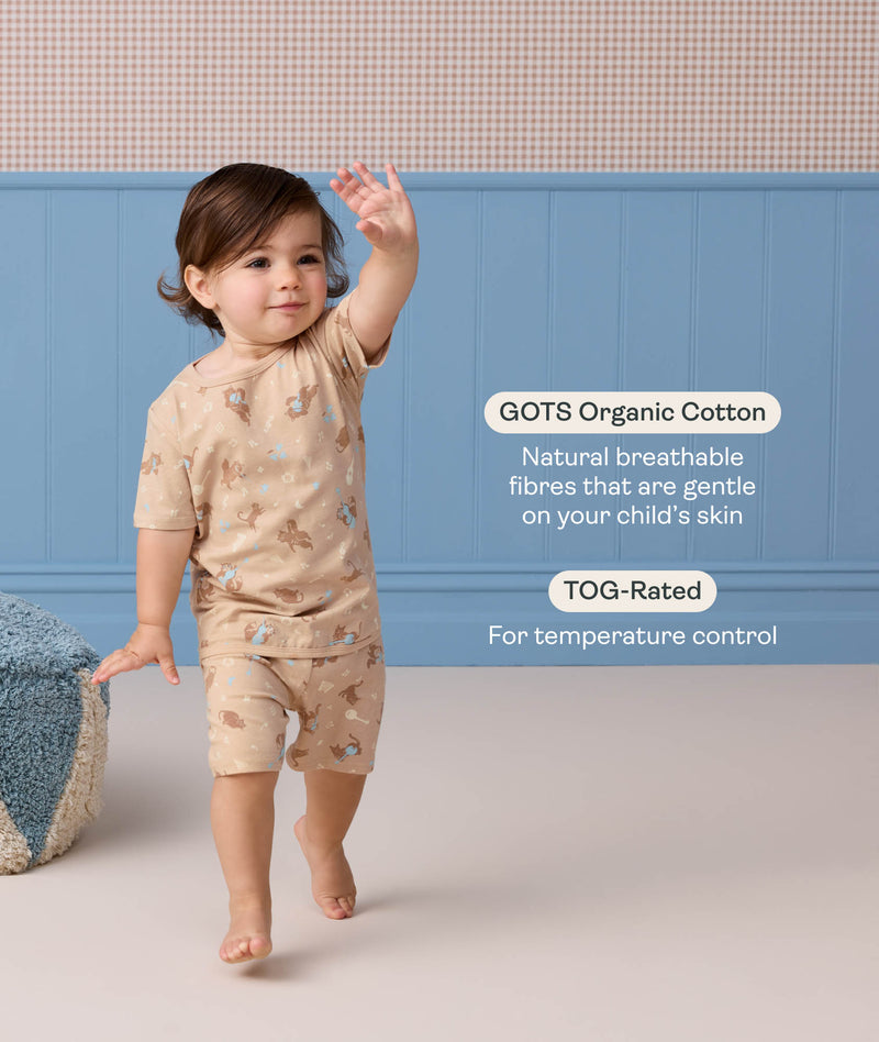 Toddler waving, wearing Short Sleeve Pyjamas, with highlighted text about GOTS-certified organic cotton and the TOG rating.