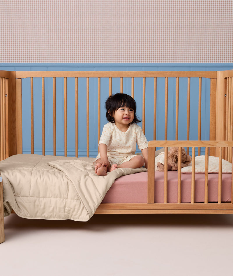 Toddler sitting in a wooden toddler bed wearing a cream patterned Short Sleeve Pyjama set.