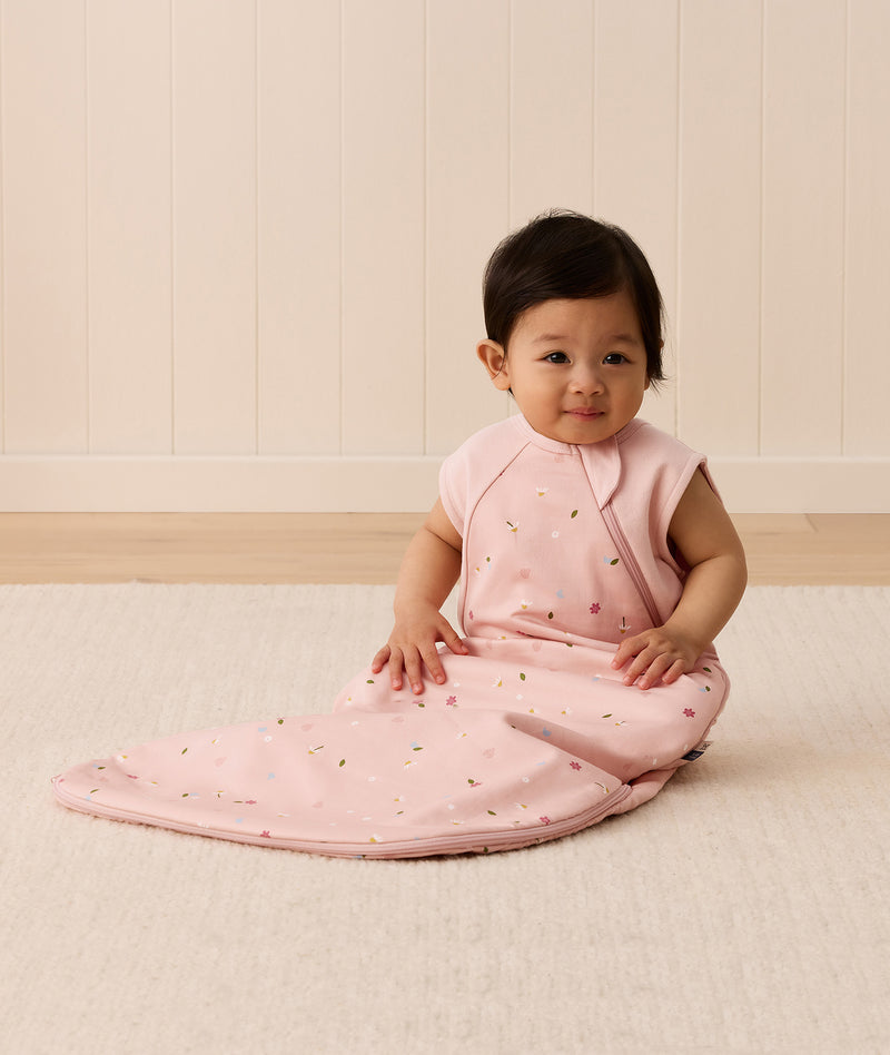 Infant sitting up in a sleeveless pink floral-patterned Sleeping Bag featuring a side zipper.