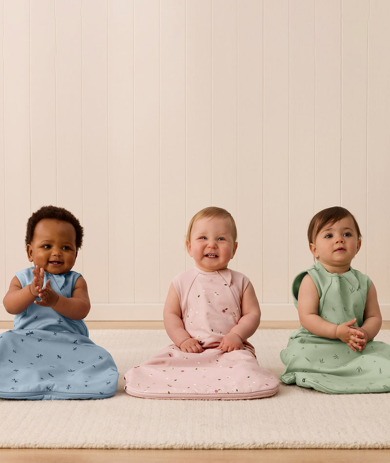 Three infants sitting side by side, wearing ergoPouch Side Zip Sleeping Bags in Dragonflies, Daisies, and Willow.