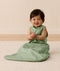 Baby sitting up in a sleeveless green leaf-patterned Sleeping Bag featuring a side zipper.