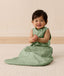 Baby sitting up in a sleeveless green leaf-patterned Sleeping Bag featuring a side zipper.