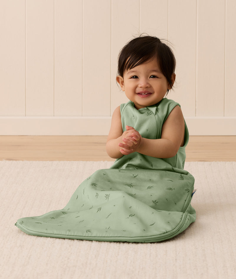 Baby sitting up in a sleeveless green leaf-patterned Sleeping Bag featuring a side zipper.