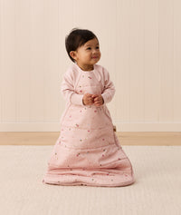 A smiling toddler wears a light pink 2.5 TOG Sleeping Bag featuring a side zipper.