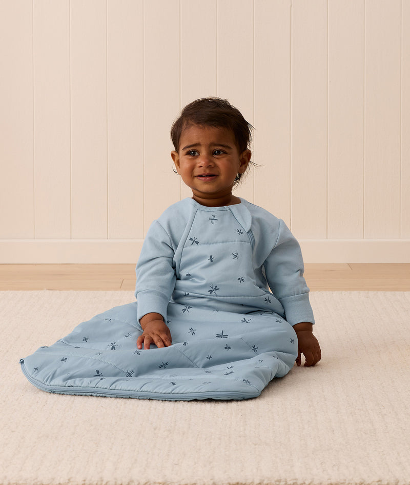 Infant sitting on the floor, wearing a Side Zip Sleeping Bag Dragonflies