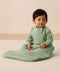 An infant sitting on a rug is wearing an ergoPouch Premium Sleeping Bag featuring side zippers.