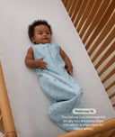 Child wrapped in a light blue cocoon swaddle lying on a cot with text about mattress fit.