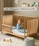 Wooden cot with sideguard and mattress, child playing inside, nursery setting.