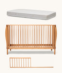 Wooden cot with mattress and safety rail on a white background