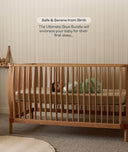 Wooden cot with a baby sleeping in it, against a neutral wall.