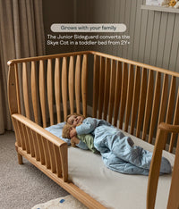 Wooden cot with a child lying inside, featuring text about the Junior Sideguard feature.