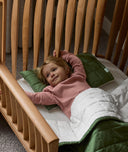 Child lying in a wooden cot with green and white bedding