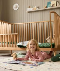 Child lying on the floor in a nursery with wooden cot and toys.