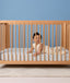Baby lying on their tummy in a wooden cot wearing a sleeveless cream printed Sleep Suit Bag.