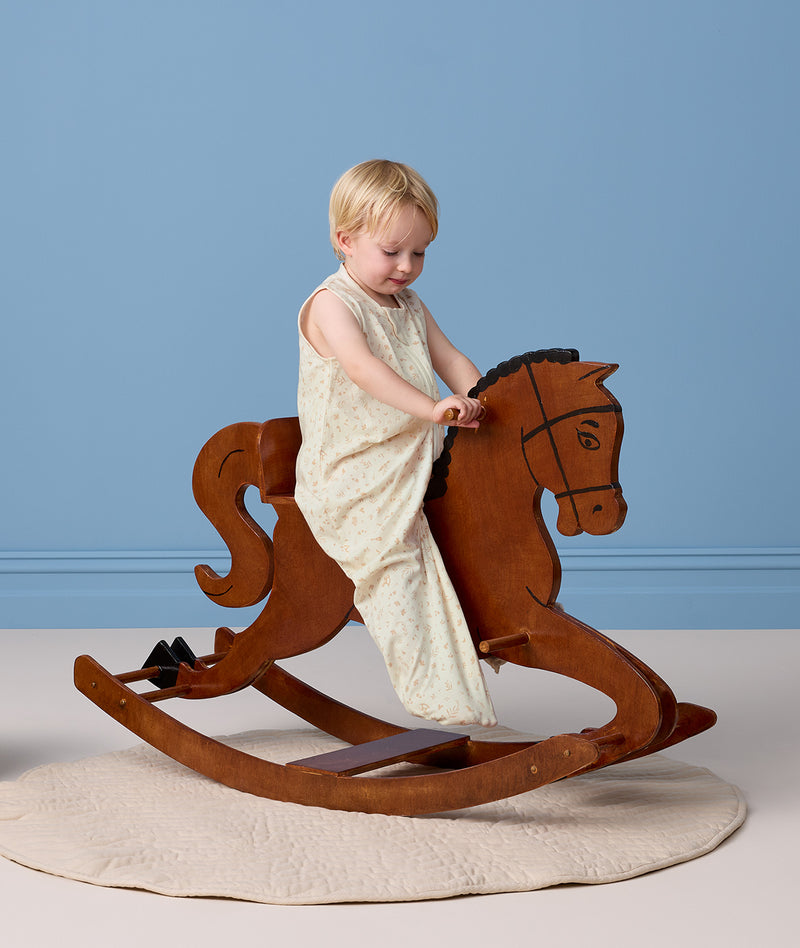 Toddler riding a wooden rocking horse wearing a sleeveless cream printed Sleep Suit Bag.