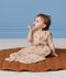 Infant sitting on a brown mat, wearing a Jersey Sleep Suit Bag 0.2 TOG made from soft, organic cotton.