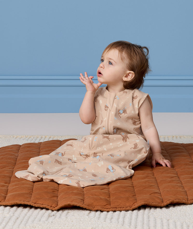 Infant sitting on a brown mat, wearing a Jersey Sleep Suit Bag 0.2 TOG made from soft, organic cotton.