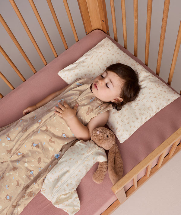 Toddler sleeping in a wooden cot wearing a beige patterned Sleep Suit Bag 0.2 TOG.