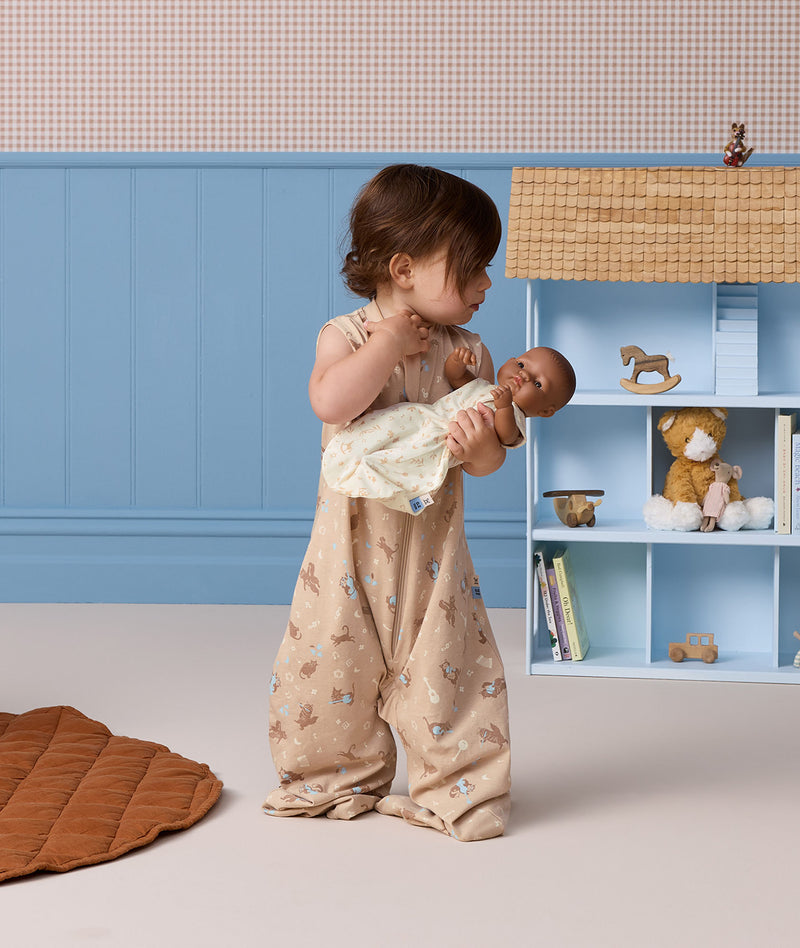 Toddler wearing a patterned sleeveless Sleep Suit Bag while holding a baby doll.