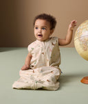 An infant is sitting next to a globe, wearing an ergoPouch Sleep Suit Bag in Savannah.
