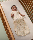 Infant lying in a cot wearing an ergoPouch Sleep Suit Bag, featuring colourful animal print