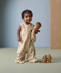 Toddler stands smiling, wearing a safari-themed Sleep Suit with legs, holding a baby doll dressed in a matching doll-sized sleeping bag with the same animal pattern.