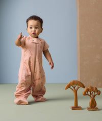 Toddler standing and pointing his fingers. He is wearing a peach-colored sleep suit bag with a subtle elephant print.