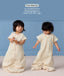 Toddler wearing cream convertible sleep suit bag, demonstrating the bag mode on the left and separate legs mode on the right.