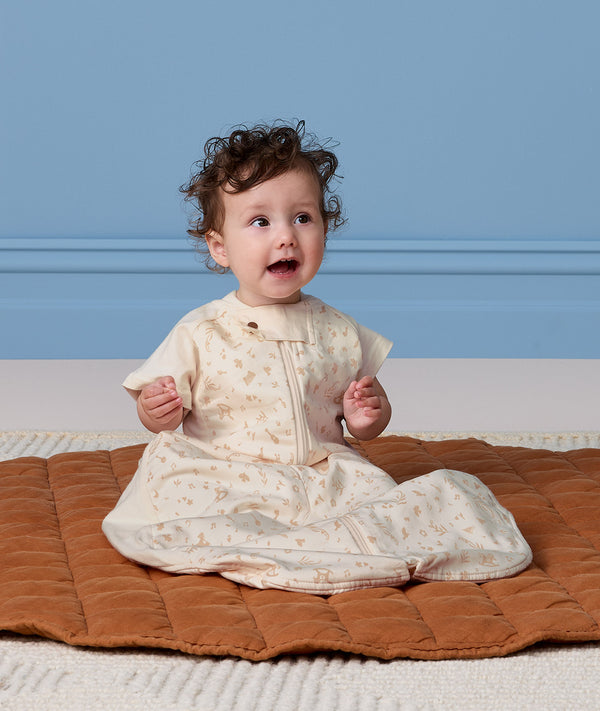 Infant sitting on a brown mat, wearing a cream Sleep Suit Bag 1.0 TOG made from organic cotton.