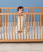 Baby standing in a wooden crib wearing a cream patterned Sleep Suit Bag with legs.