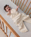 Baby reaching up while lying in a wooden cot, wearing a convertible sleep suit bag with leg openings.